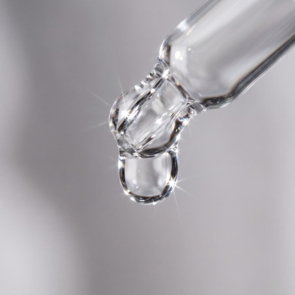 Gotero de vidrio soltando una gota de serum completamente transparente